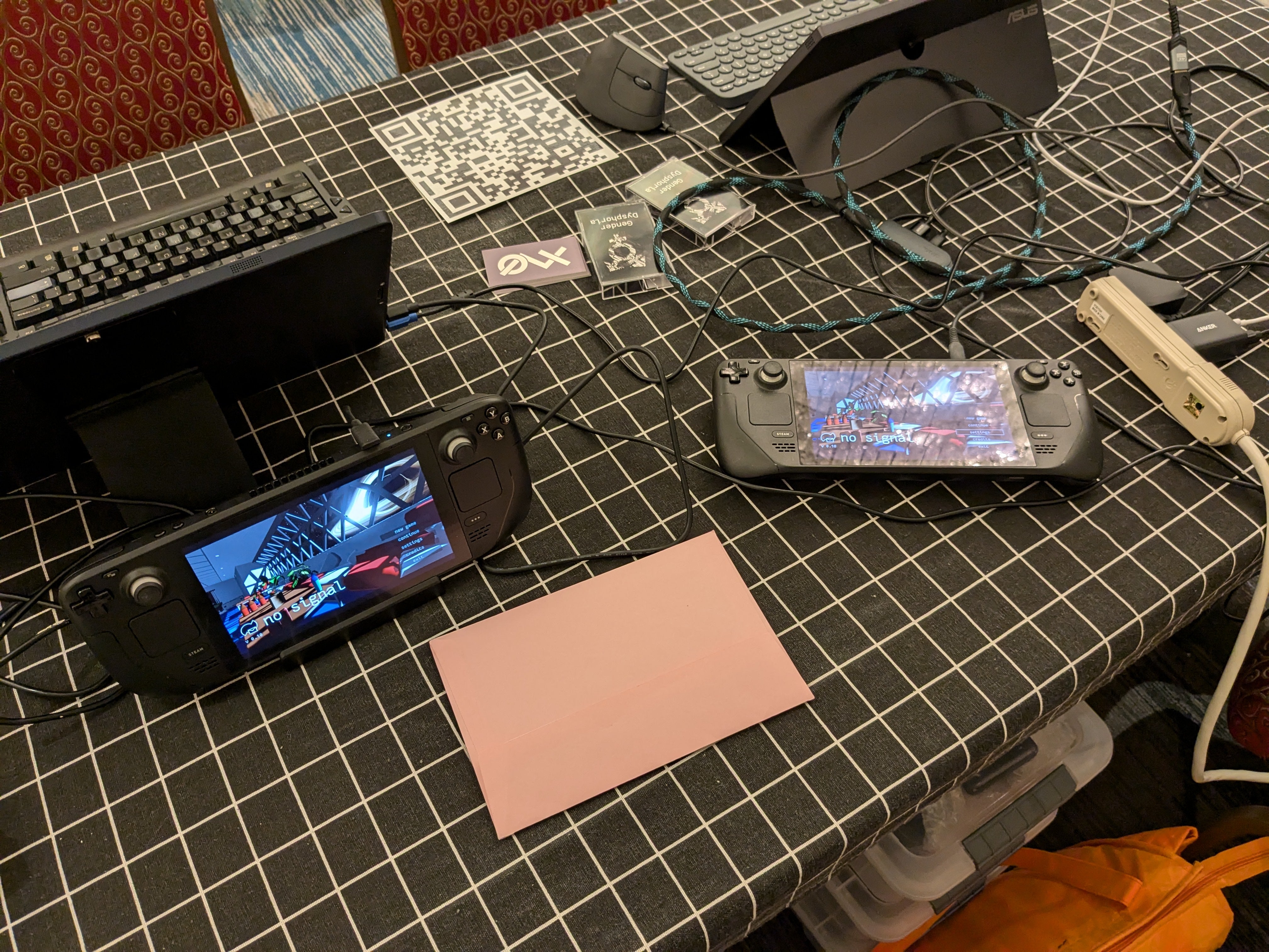 The setup from behind the table, where two Steam Decks can be seen, mirroring the displays that the players can see. There is also a pink envelope on the table with no signal bookmarks inside of it.